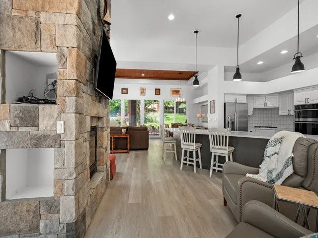 Stone-clad fireplace with built-in niches, light wood-finish flooring, recessed lighting, kitchen island with seating, and white cabinetry