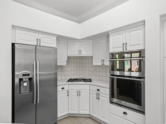 White cabinetry with dark hardware, stainless steel side-by-side refrigerator, gas cooktop, double wall ovens, and light-toned backsplash