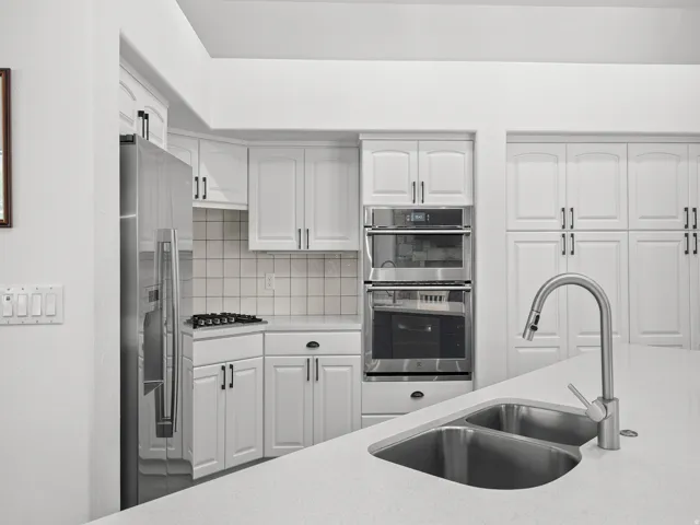 Modern kitchen with white cabinetry, stainless steel appliances, double basin sink, and solid surface countertops