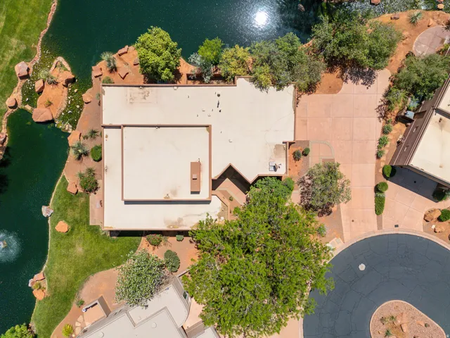 Property featuring a flat roofline, extensive paved driveway, mature trees, and a water feature