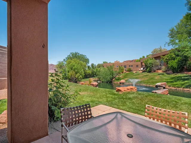 Patio with concrete flooring, stucco exterior wall, and direct access to a water feature with a fountain, surrounded by green landscaping