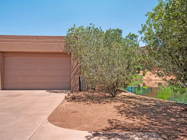 Stucco exterior with a garage door, featuring a concrete driveway, and natural landscaping with mature trees, bordering a tranquil body of water