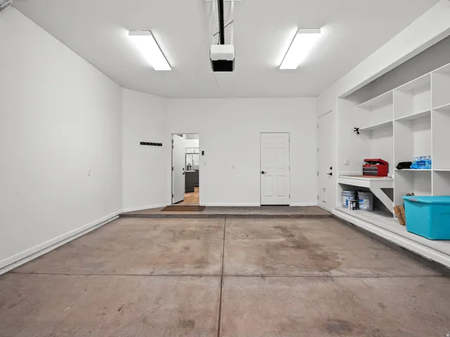 Attached garage with concrete flooring, built-in shelving, workbench, and overhead fluorescent lighting