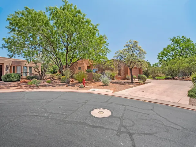 Stucco exterior with mature trees, desert landscaping, and an attached garage