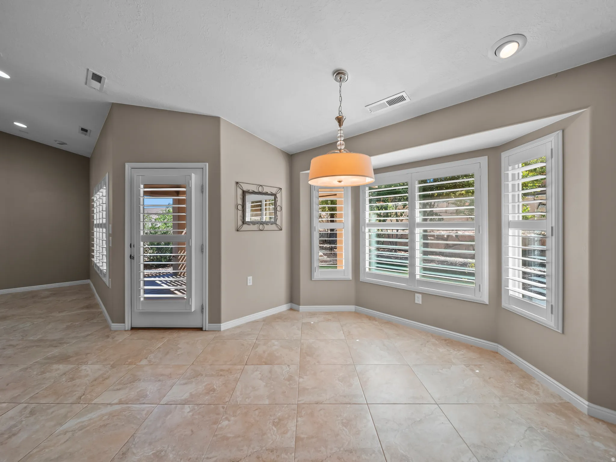 Bay window with plantation shutters, recessed lighting, vaulted ceiling, tile flooring, and a decorative pendant light fixture