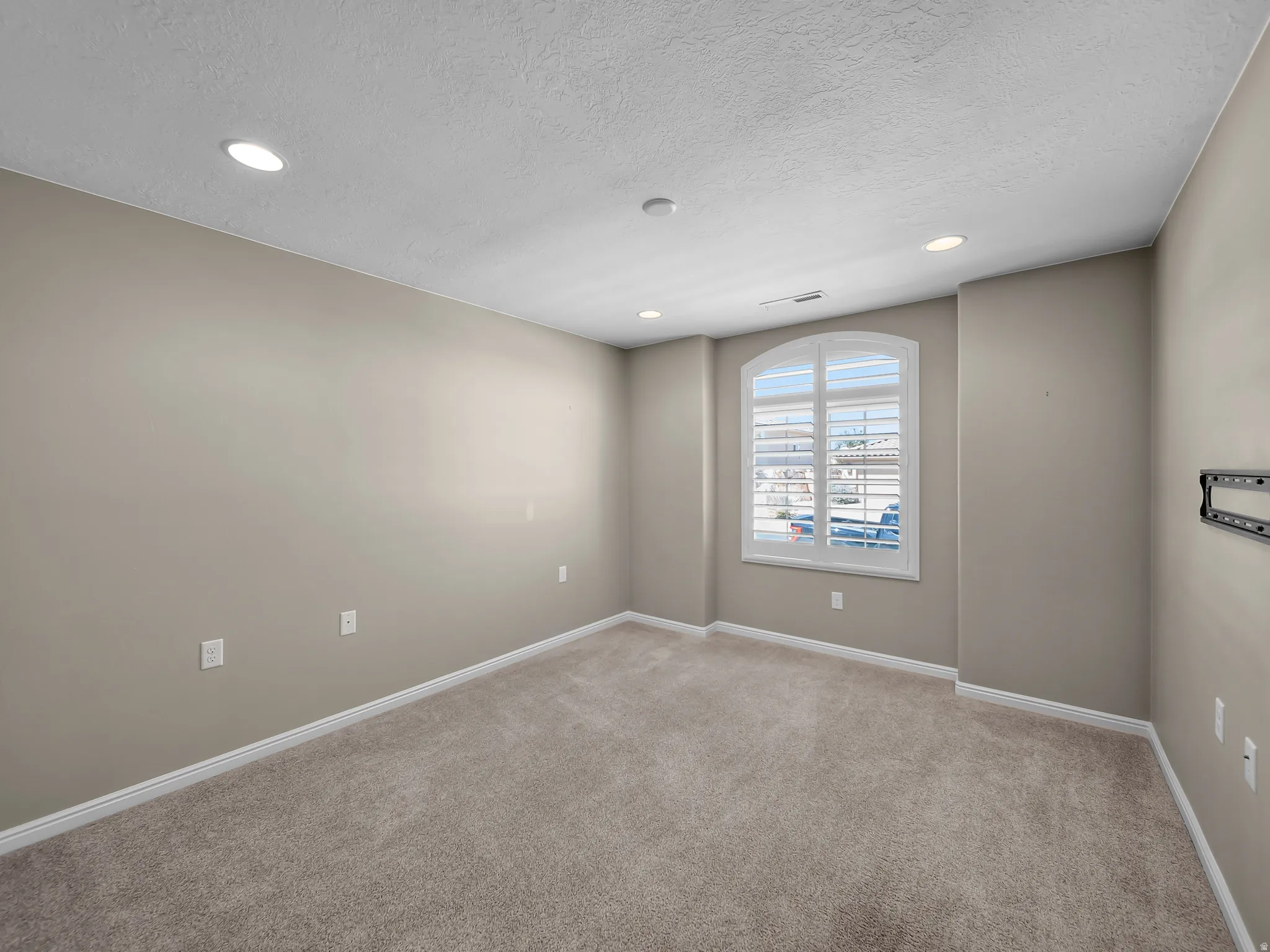 Arched window with plantation shutters, recessed ceiling lighting, textured ceiling, light-toned carpeting, and painted walls