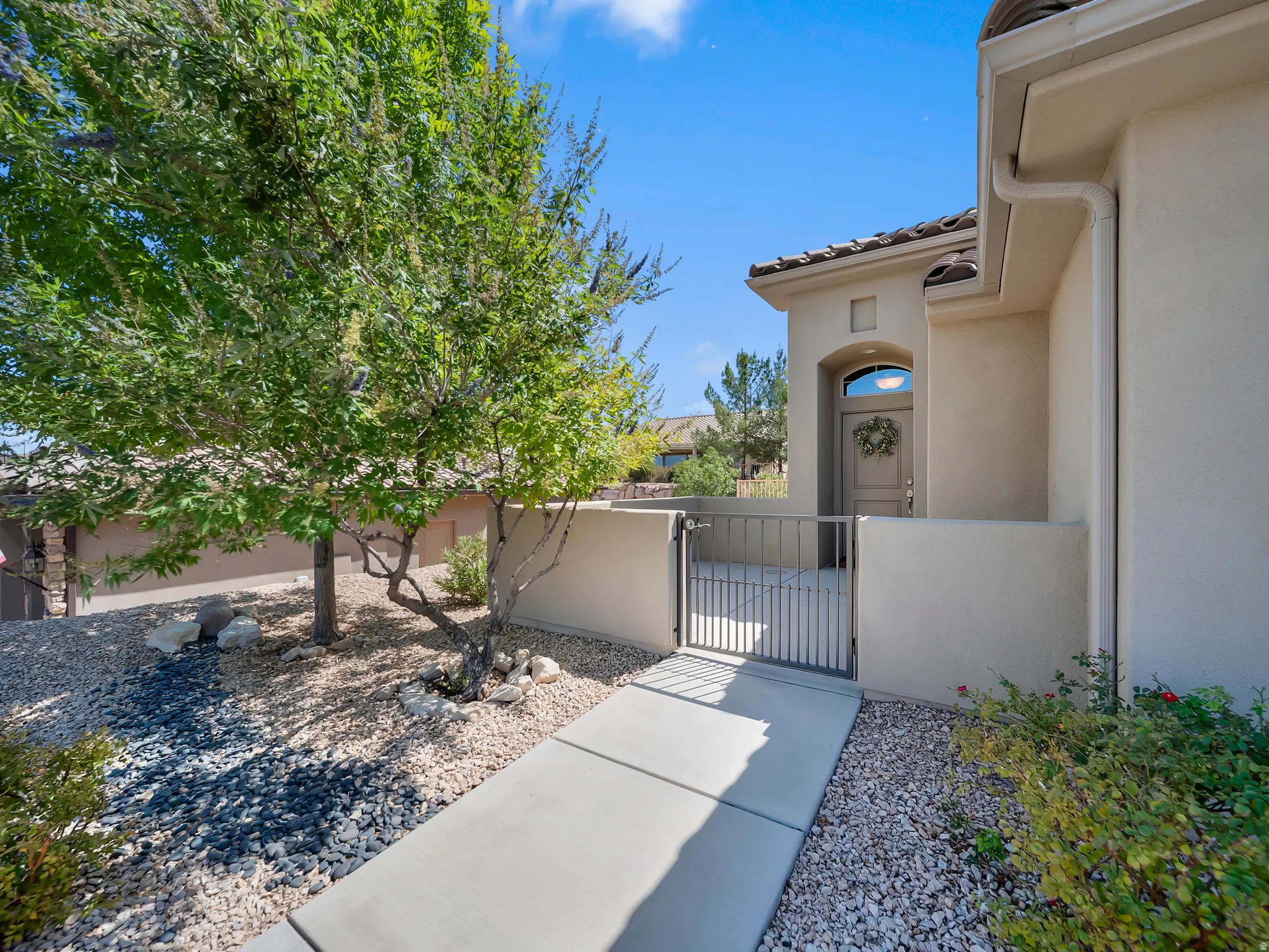 Arched entry door with transom window, tile roof, stucco exterior, paved walkway, and decorative metal gate