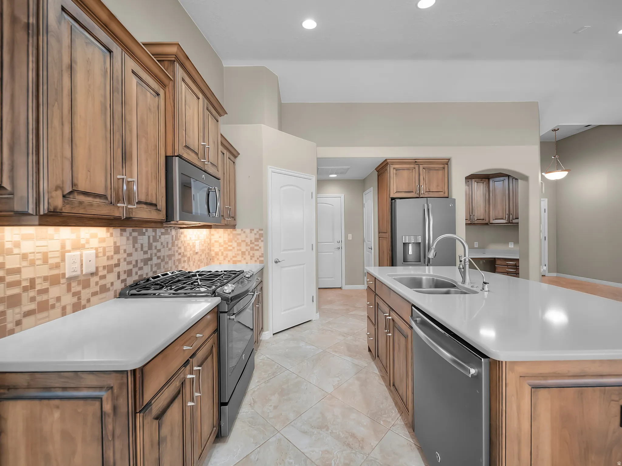 Kitchen featuring wood cabinetry, stainless steel appliances, a tiled backsplash, a kitchen island with a sink, and tile flooring