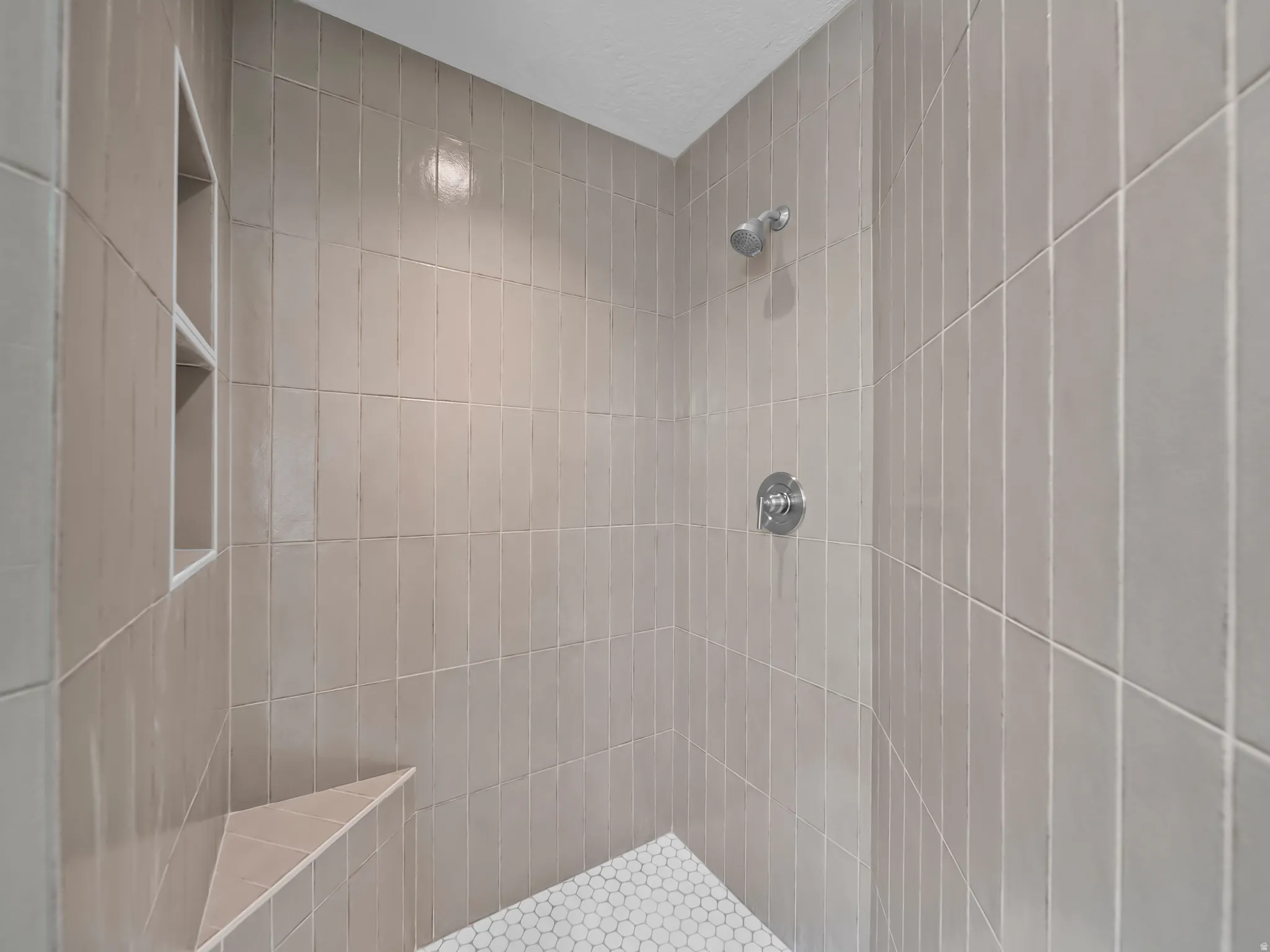 Shower with vertical subway tile, integrated shower niche, built-in bench, and hexagonal floor tiles