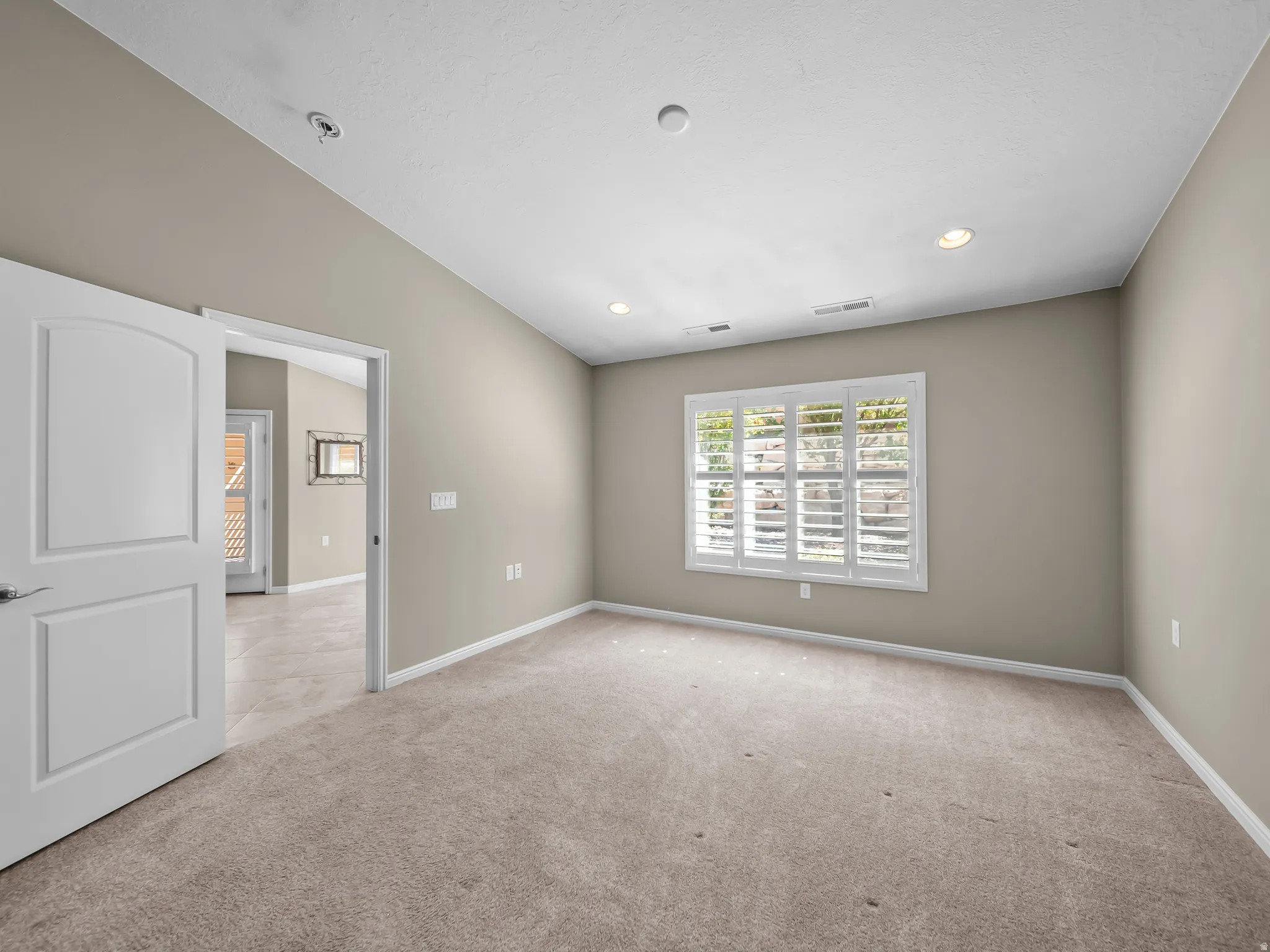 Vaulted ceiling with recessed lighting, neutral wall paint, carpet flooring, a window with plantation shutters, and a paneled interior door