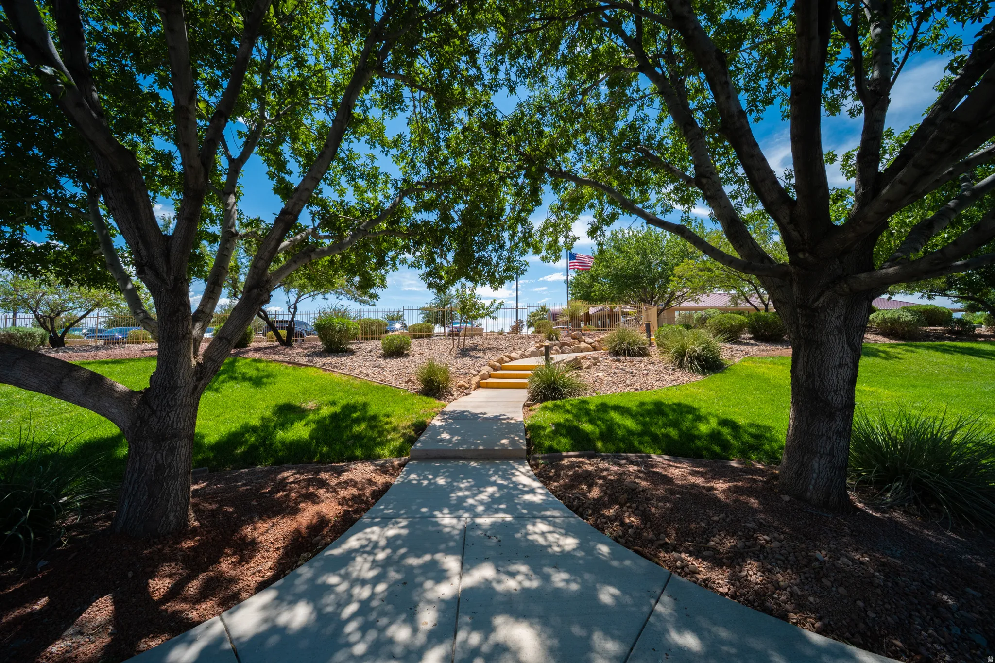 Manicured grounds featuring mature trees, a concrete pathway, and landscaped areas with shrubs and ground cover