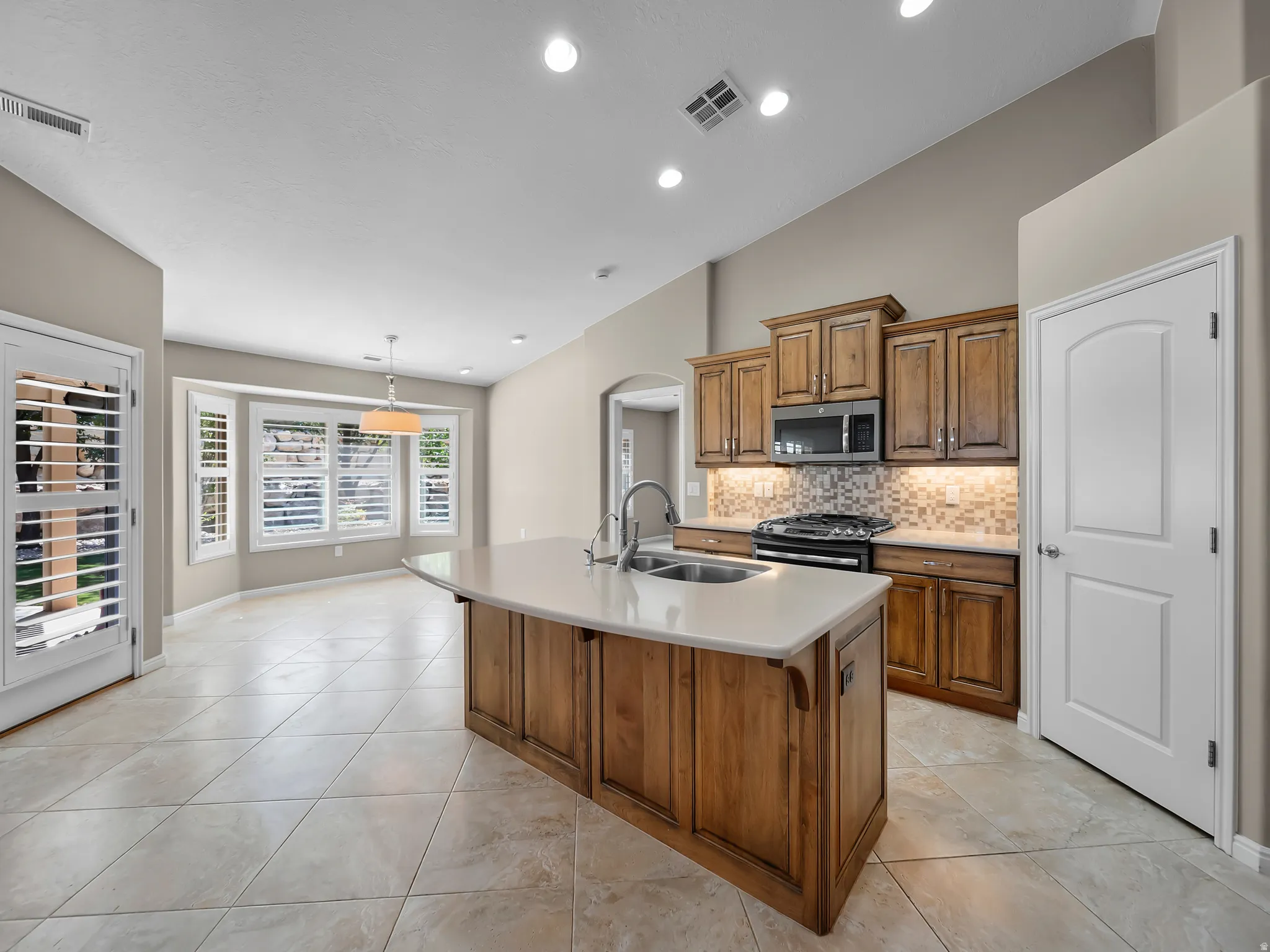 Kitchen featuring wood cabinetry, stainless steel appliances, a center island with sink, and tile flooring