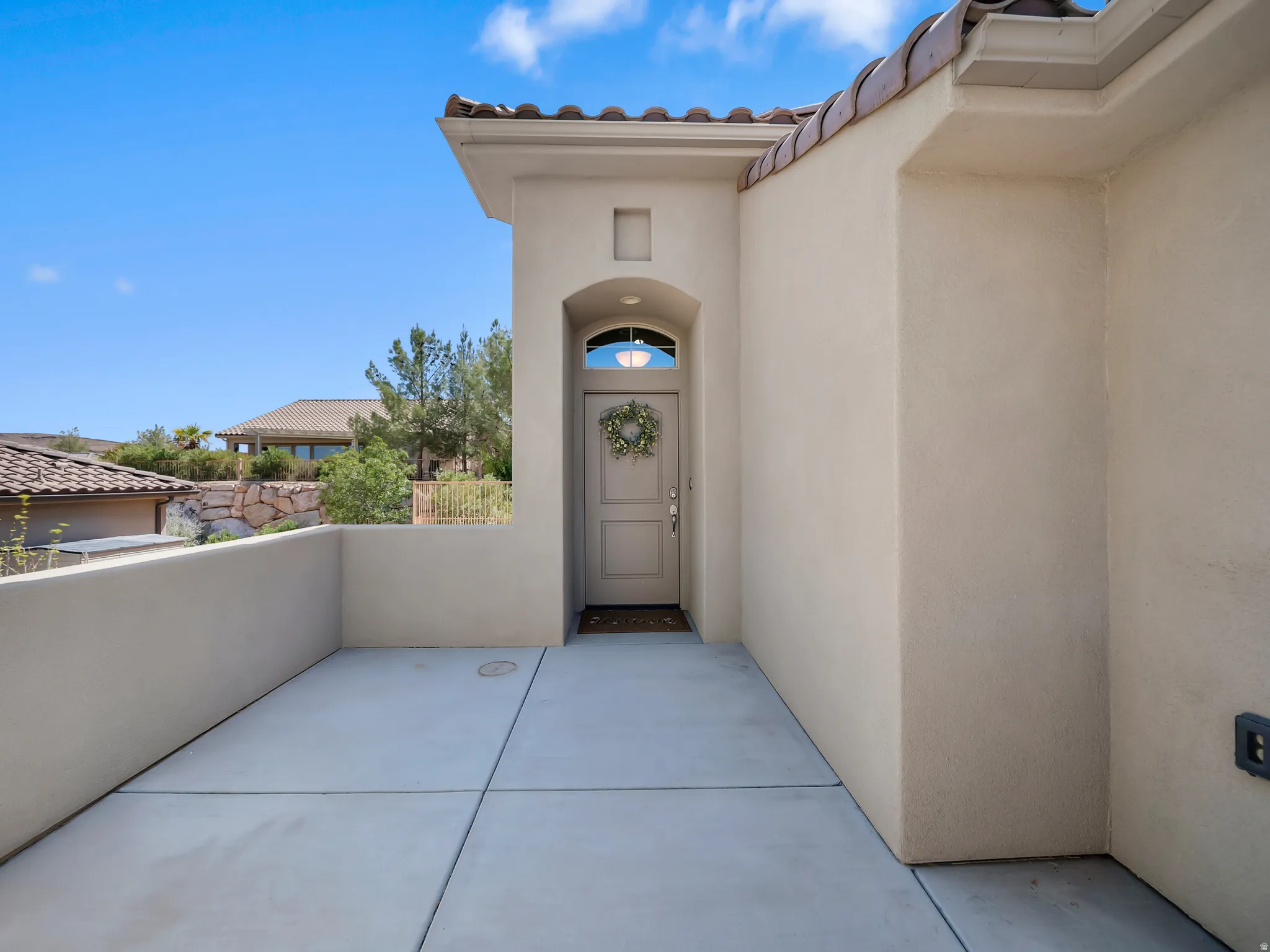 Entryway featuring a stucco exterior, concrete patio, arched transom window, and tile roofing
