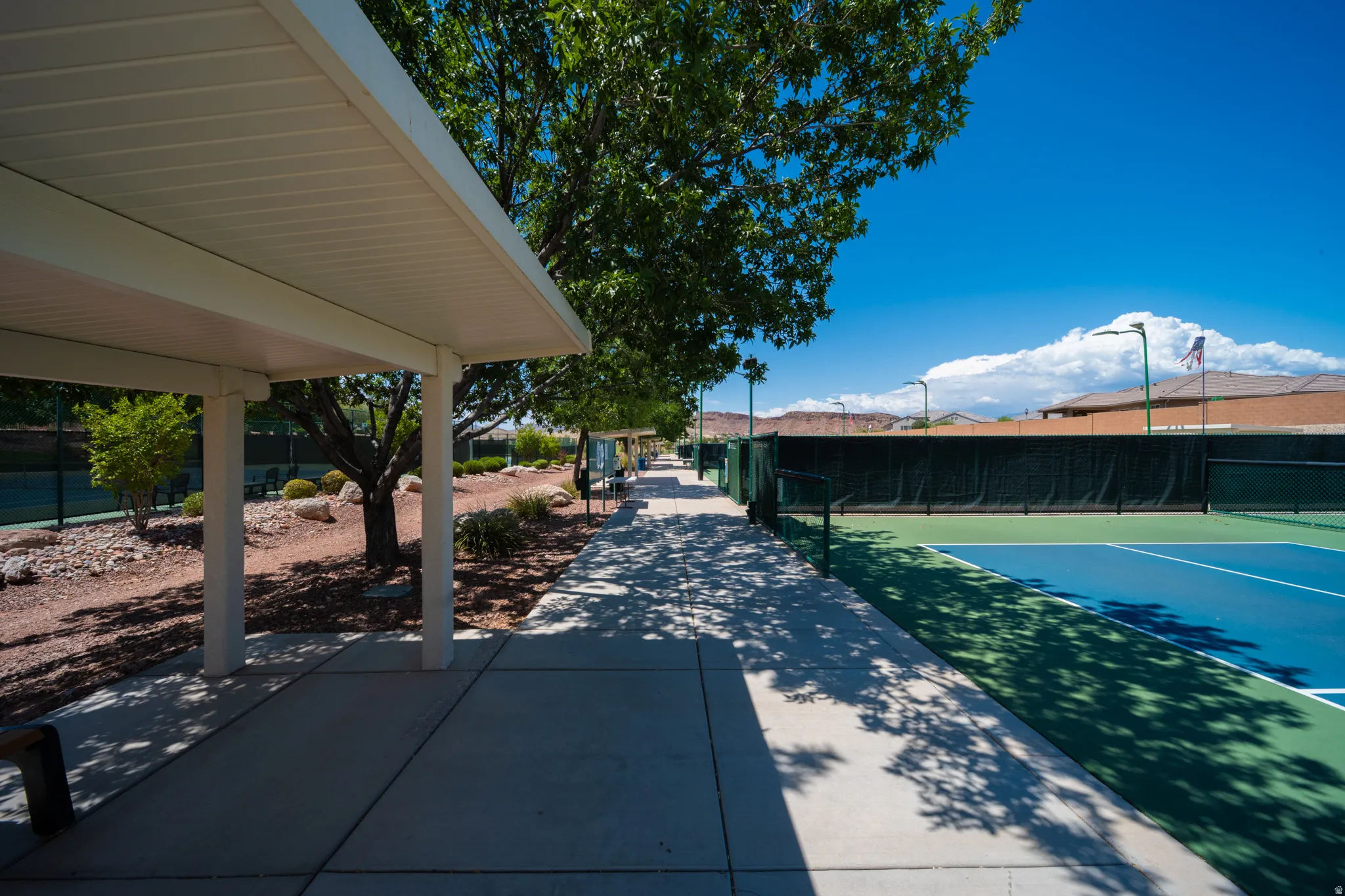 Covered walkway with an adjacent hard surface tennis court and surrounding landscape