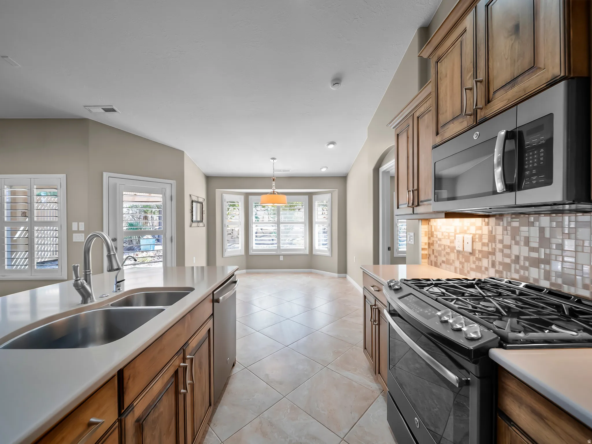 Kitchen featuring a double basin stainless steel sink, gas range, built-in microwave, wood-finish cabinetry, and tile flooring