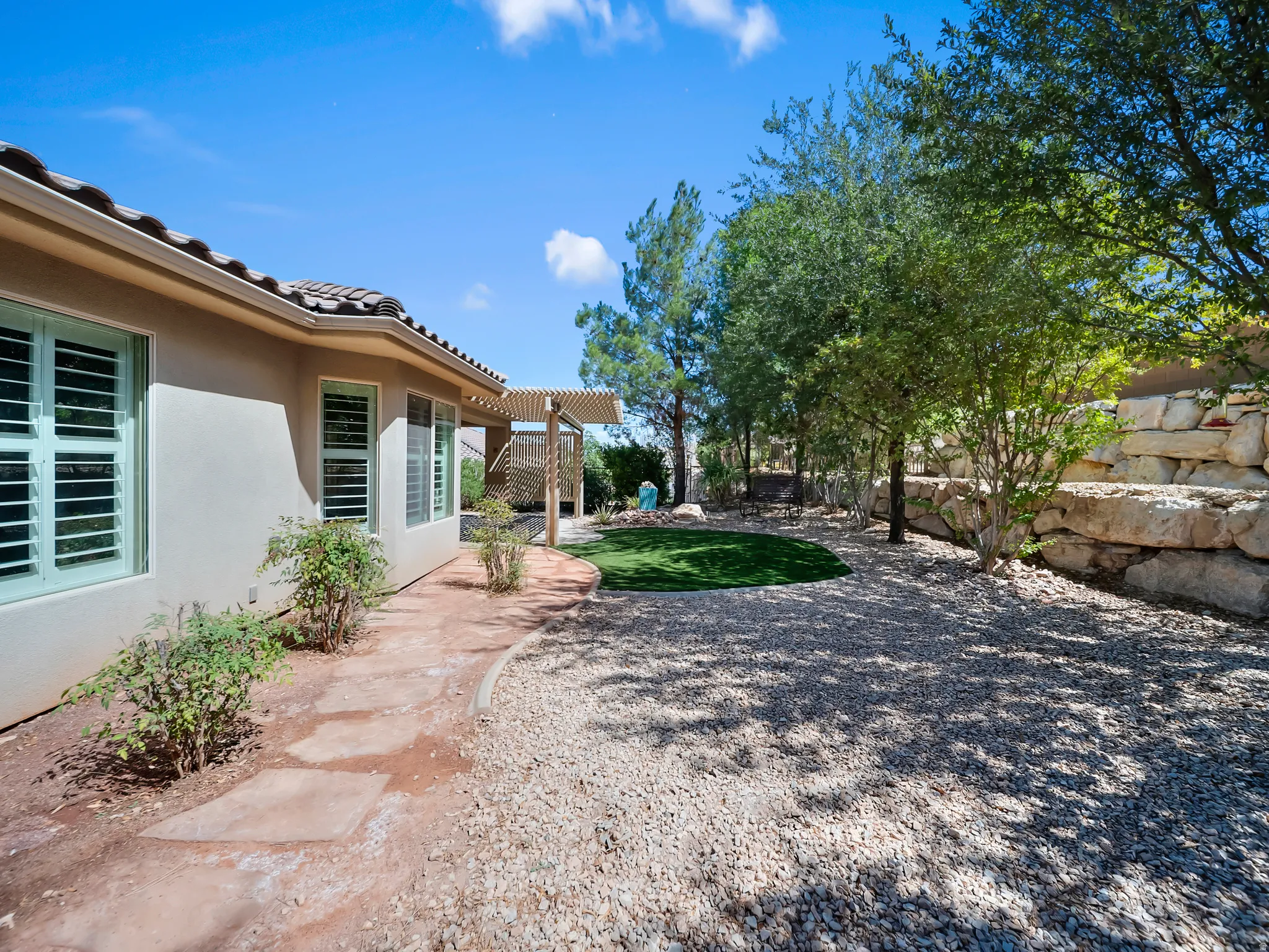 Exterior stucco finish, tile roof, window shutters, flagstone pathway, gravel landscaping, terraced stone retaining wall, artificial turf area