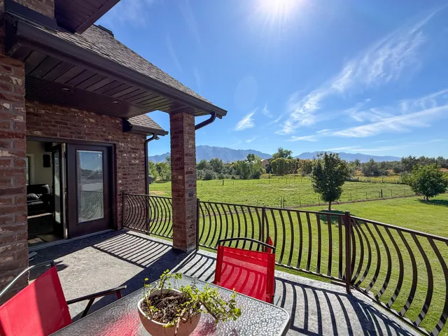 Brick exterior with covered patio, decorative metal railing, and double French doors opening to an expansive green landscape