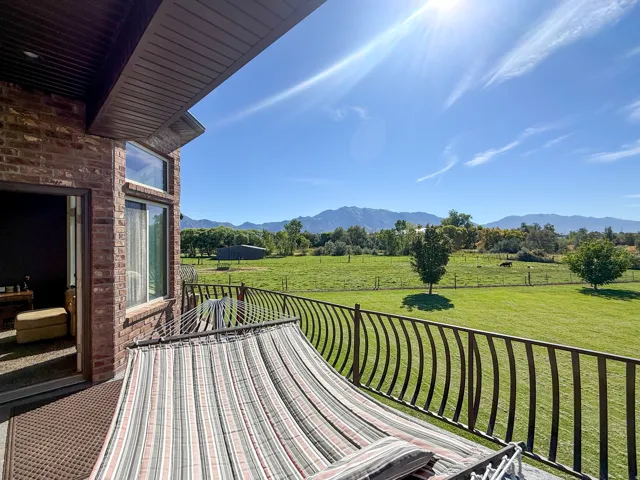 Private outdoor balcony featuring a decorative metal railing, brick exterior, and expansive green landscape