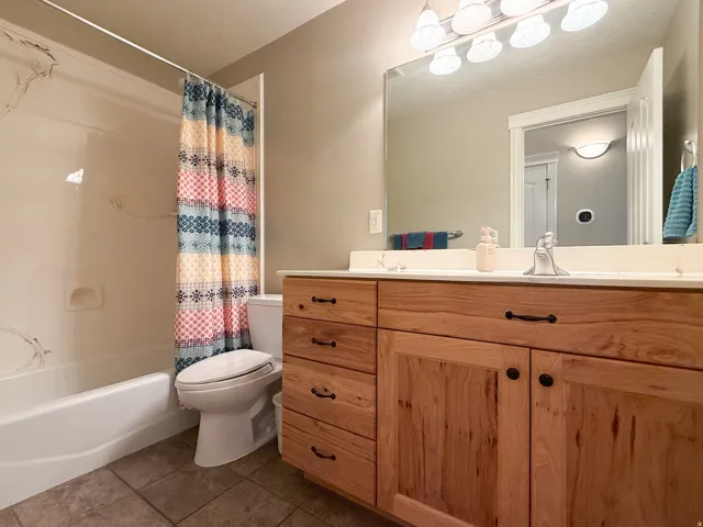Light wood-finish vanity with dark hardware, a white countertop, and an integrated sink