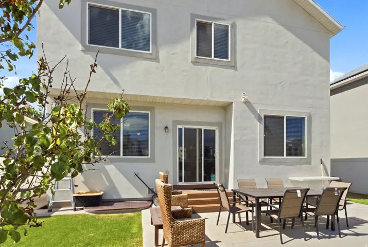 Rear exterior with a concrete patio, sliding glass door access, exterior lighting, wood steps, and a stucco finish