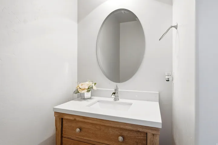 Oval mirror, wood-finish vanity with drawer storage, integrated sink, and chrome-finish faucet
