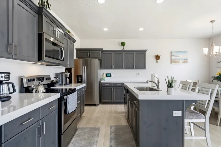 Kitchen featuring dark-toned cabinetry, stainless steel appliances, light countertops, wood-finish flooring, and recessed ceiling lighting
