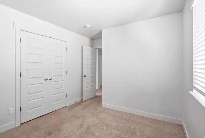 White walls, light-toned carpeting, white interior doors, and a window with horizontal blinds