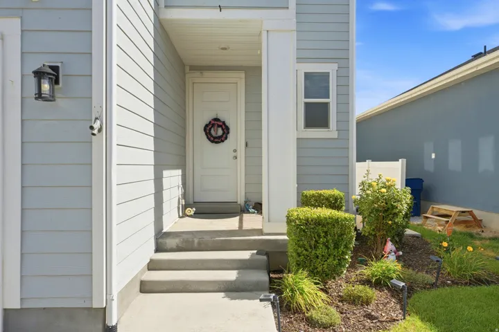 Light blue siding with white trim, covered entryway, multi-step concrete porch, exterior lighting fixture, and a planted garden bed
