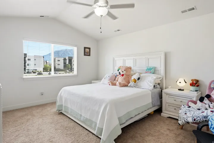 Vaulted ceiling with a ceiling fan, white paneled headboard, and a large window