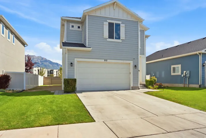 Light blue siding exterior with white trim, an attached garage, a concrete driveway, and a manicured lawn
