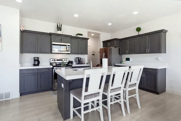 Spacious kitchen featuring dark cabinetry, stainless steel appliances, a white countertop island, and wood-finish flooring