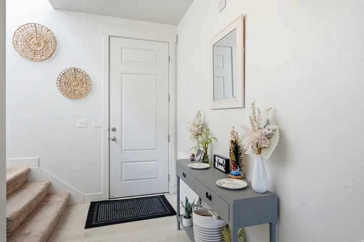 White paneled entry door, light wood-finish flooring, and a carpeted staircase