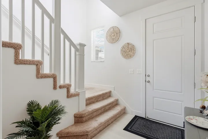 White paneled door, carpeted staircase, white banister, and a window with blinds