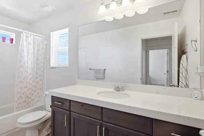 Bathroom featuring a built-in vanity with dark wood-finish cabinetry, a large integrated mirror, white countertop, and an integrated tub with shower