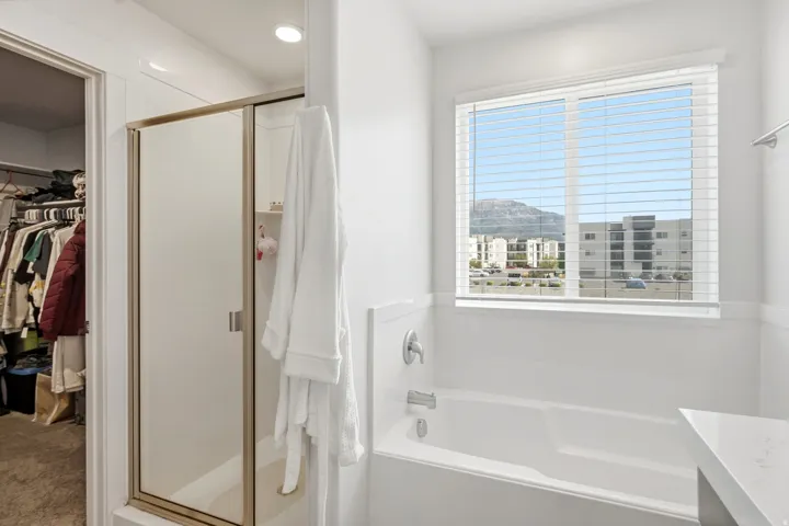 Built-in bathtub, window with horizontal blinds, mountain backdrop, and a glass-enclosed shower