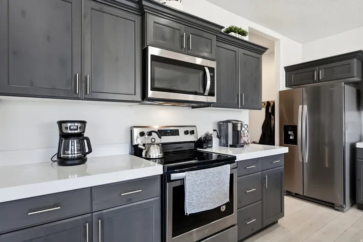 Dark wood-finish cabinetry with crown molding, stainless steel appliances, white countertops, and light wood-finish flooring