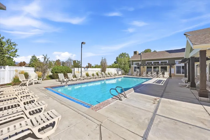 Outdoor swimming pool surrounded by concrete decking, featuring a perimeter fence and mature landscaping