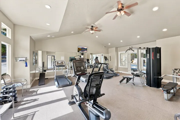 Spacious fitness center featuring varied exercise equipment, vaulted ceilings, recessed lighting, and wall-mounted mirrors