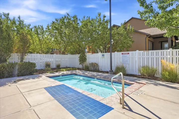 Swimming pool with blue mosaic tile accents, concrete surround, white privacy fencing, and mature landscaping
