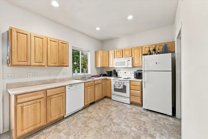 Kitchen featuring light wood-finish cabinetry, white appliances, recessed lighting, and a window above the sink
