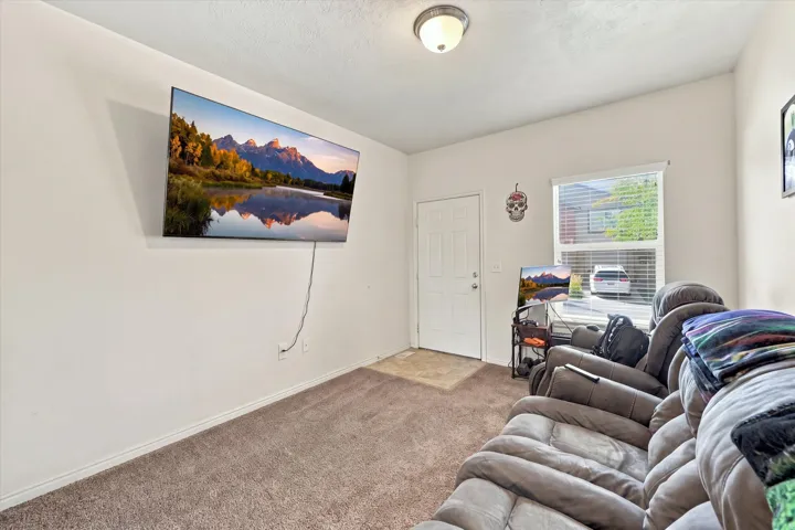 Wall-mounted light fixture, white interior door, window with blinds, and neutral tone carpet