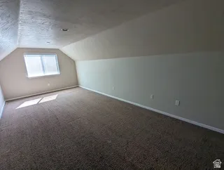 Carpeted room featuring a window with blinds, angled ceiling, and neutral wall tones