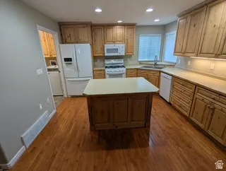 Kitchen featuring wood-finish flooring, natural wood cabinetry, a central island with a solid surface countertop, recessed lighting, and a bay window