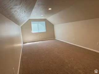 Carpeted room with sloped ceilings, recessed lighting, and a single window