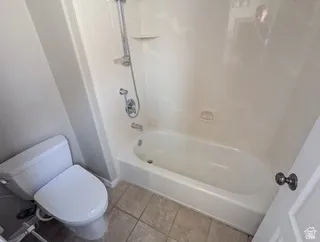 White bathtub with an integrated shower, chrome fixtures, and a white toilet