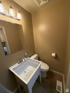 Wall-mounted vanity mirror with an overhead three-light fixture, white utility sink, and a white toilet