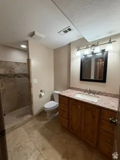 Walk-in shower with natural stone tile, wood-finish vanity with ample storage, granite-style countertop, and tile flooring