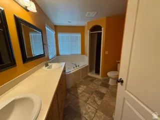 Dual sink vanity with light-toned countertop, jetted tub, separate shower enclosure with arched entry, and tiled flooring
