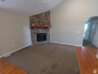 Vaulted ceilings with recessed lighting, a stone-faced fireplace with a wood mantle, and a combination of wood-finish flooring and carpet