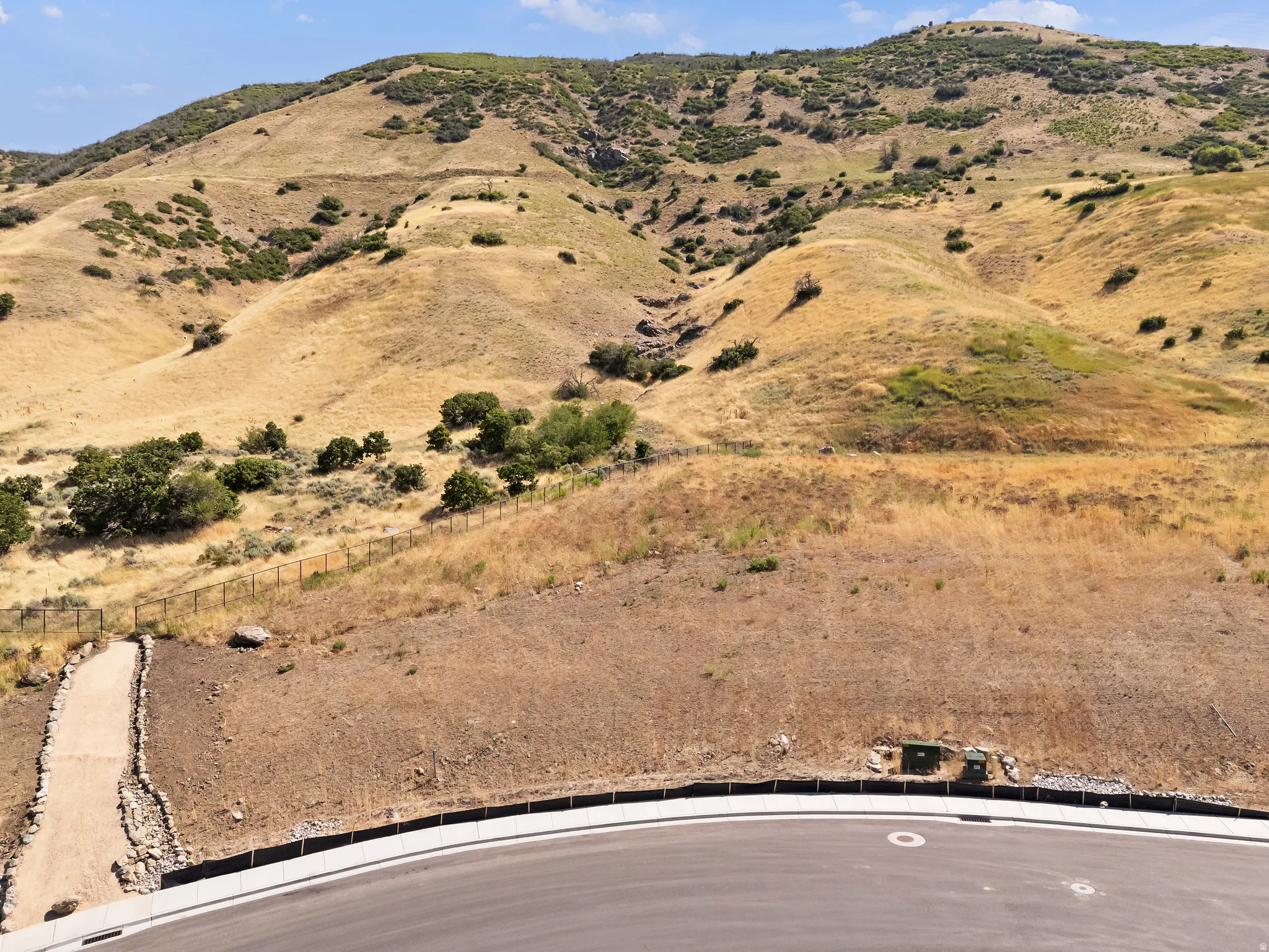 Graded lot with an asphalt road, a rock-lined pathway, and a wire fence